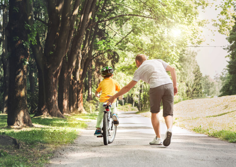 自転車に乗る練習をしている子どもとそれを後ろからサポートする父親の写真