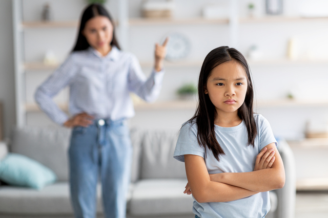 不機嫌そうな女の子の後ろで、母親が怒っている。