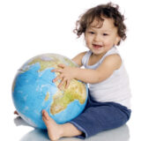 2歳くらいの男の子が地球の模型を座って持って、微笑んでいる。