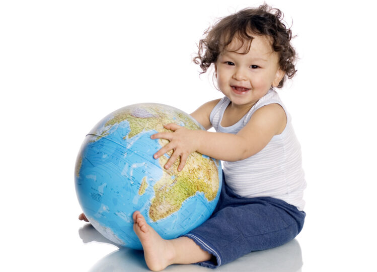 2歳くらいの男の子が地球の模型を座って持って、微笑んでいる。