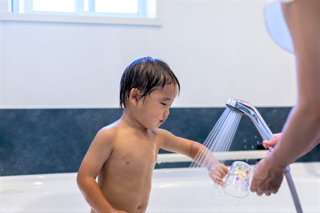 男の子がお風呂場でシャワーを腕に当てている。