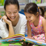 母親と女の子が一緒に笑顔で絵本を読んでいる。