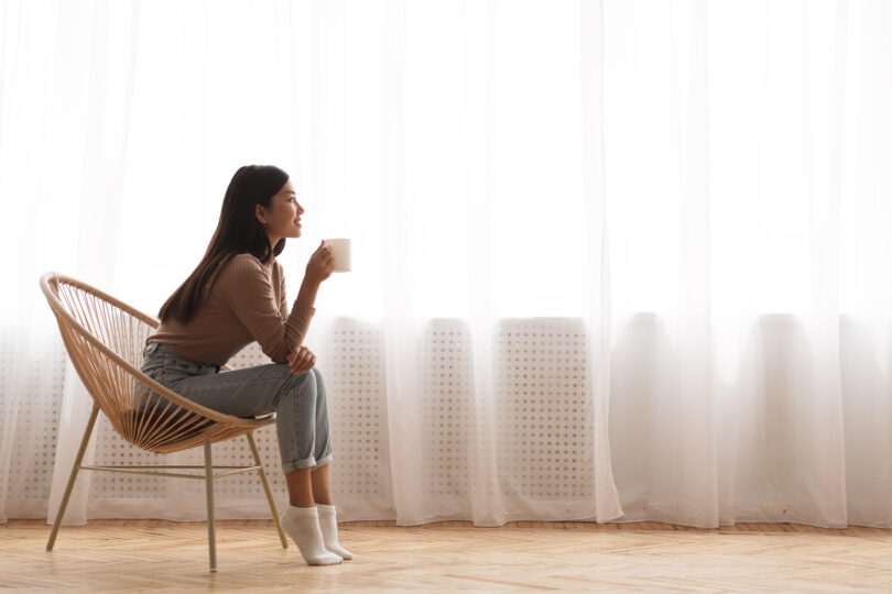 女性が椅子に座って、リラックスした様子でコーヒーを飲んでいる。