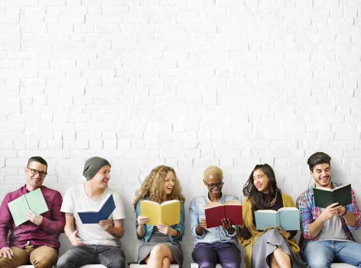 いろいろな人種の大人6人が本を読みながら談笑している。