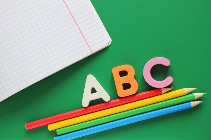 緑の背景にカラフルな色鉛筆とABCの文字が置いてある。