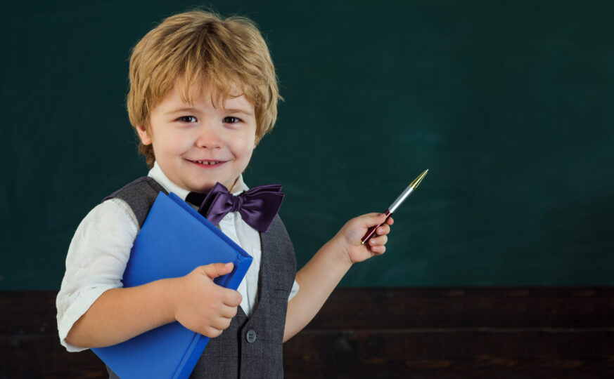 3歳くらいの男の子が黒板の前に立ち、ペンで黒板を指している。
