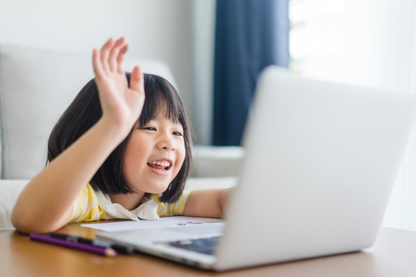 女の子がオンラインレッスンを受けながら手を挙げている。
