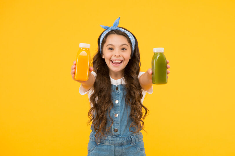 女の子が2つのスムージーを両手に持って笑っている。