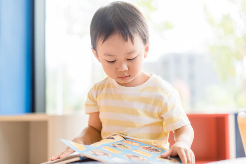 4歳くらいの男の子が家で英語の本を見ている。