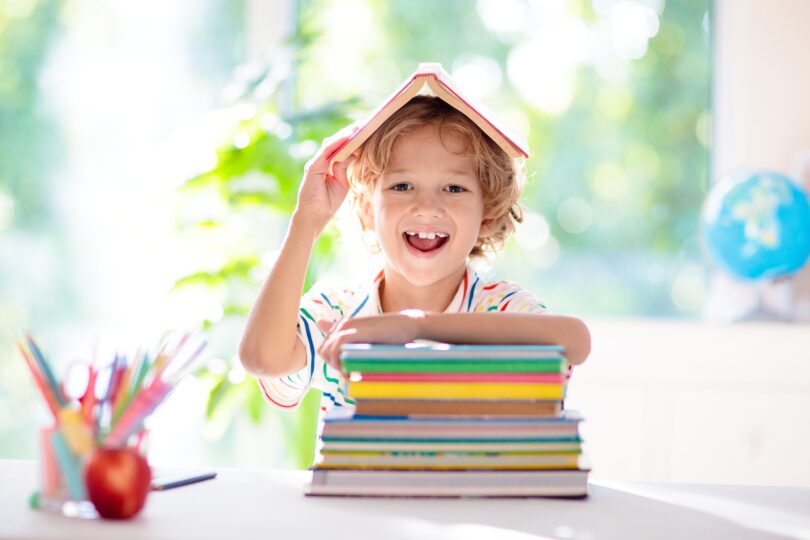 小学生の男の子が机に向かい、頭の上に本をのせて笑っている。