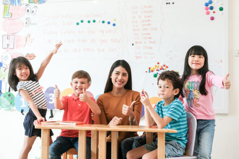 アジア人の女性の先生を小学生の子どもたちが囲んでいる英会話教室。