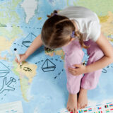 女の子が世界地図の上に座って書き込みをしている。