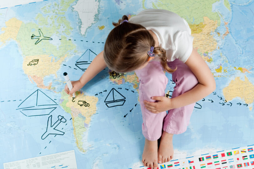 女の子が世界地図の上に座って書き込みをしている。
