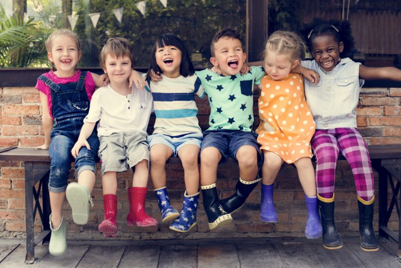 いろいろな人種の子どもがベンチに座って笑っている。