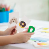 子どもの手が犬の絵とドーナッツの絵を左手に握り、Dのアルファベットを右手に握っている。