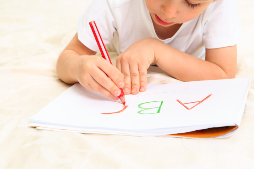 小さな男の子が白い紙にアルファベットを書いている。